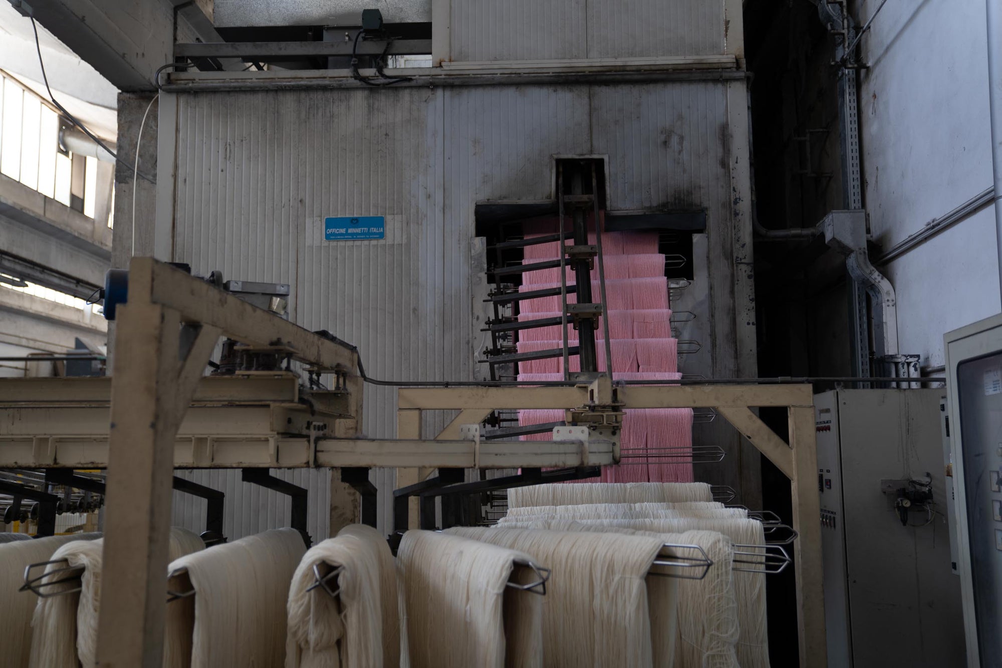 White and pink hanks of Merino wool on metal rods being mechanically transported into the drying oven.