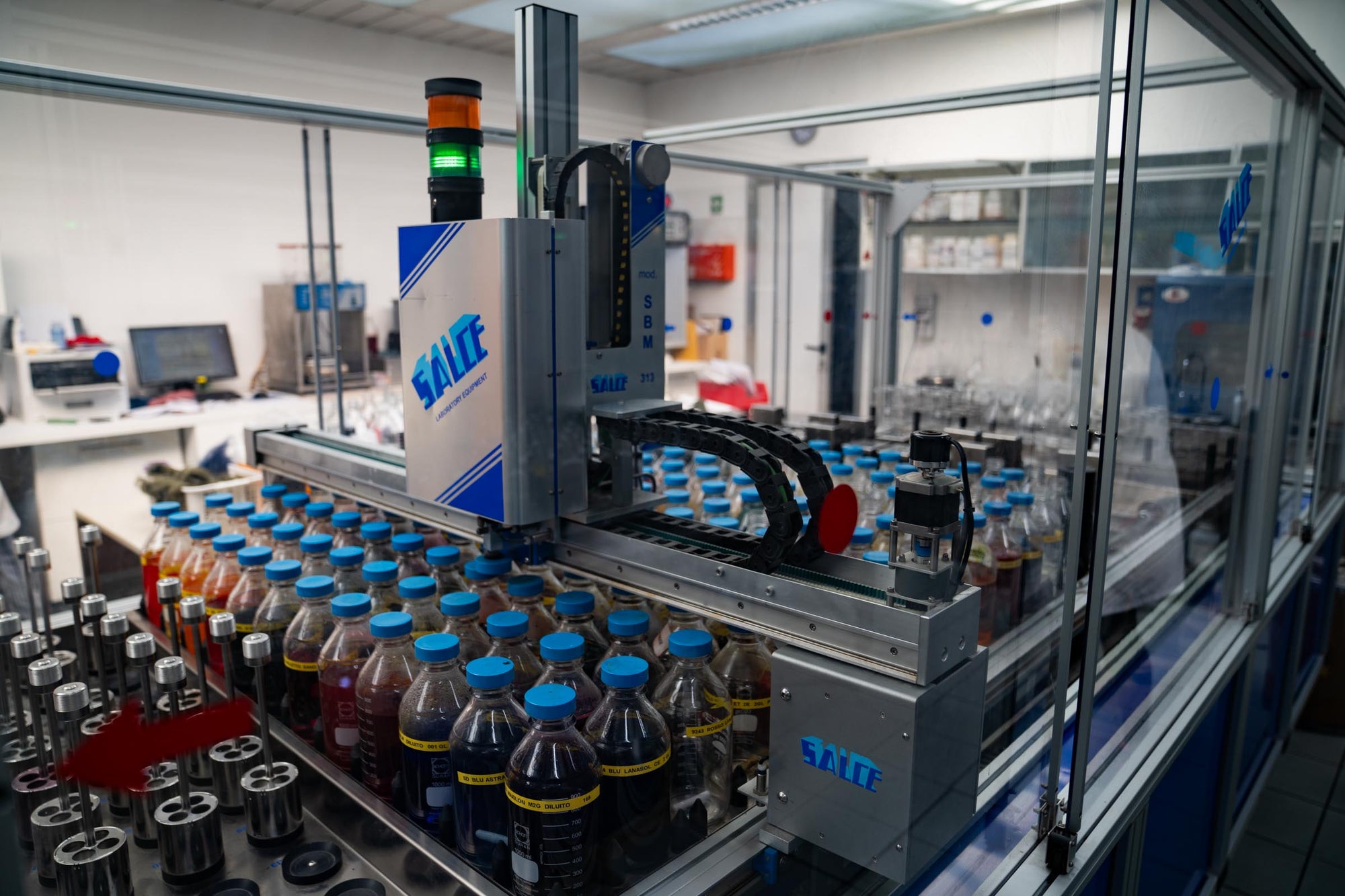 A robot arm filling bottles with dye colors in a lab installation at Tintoria Ferraris.