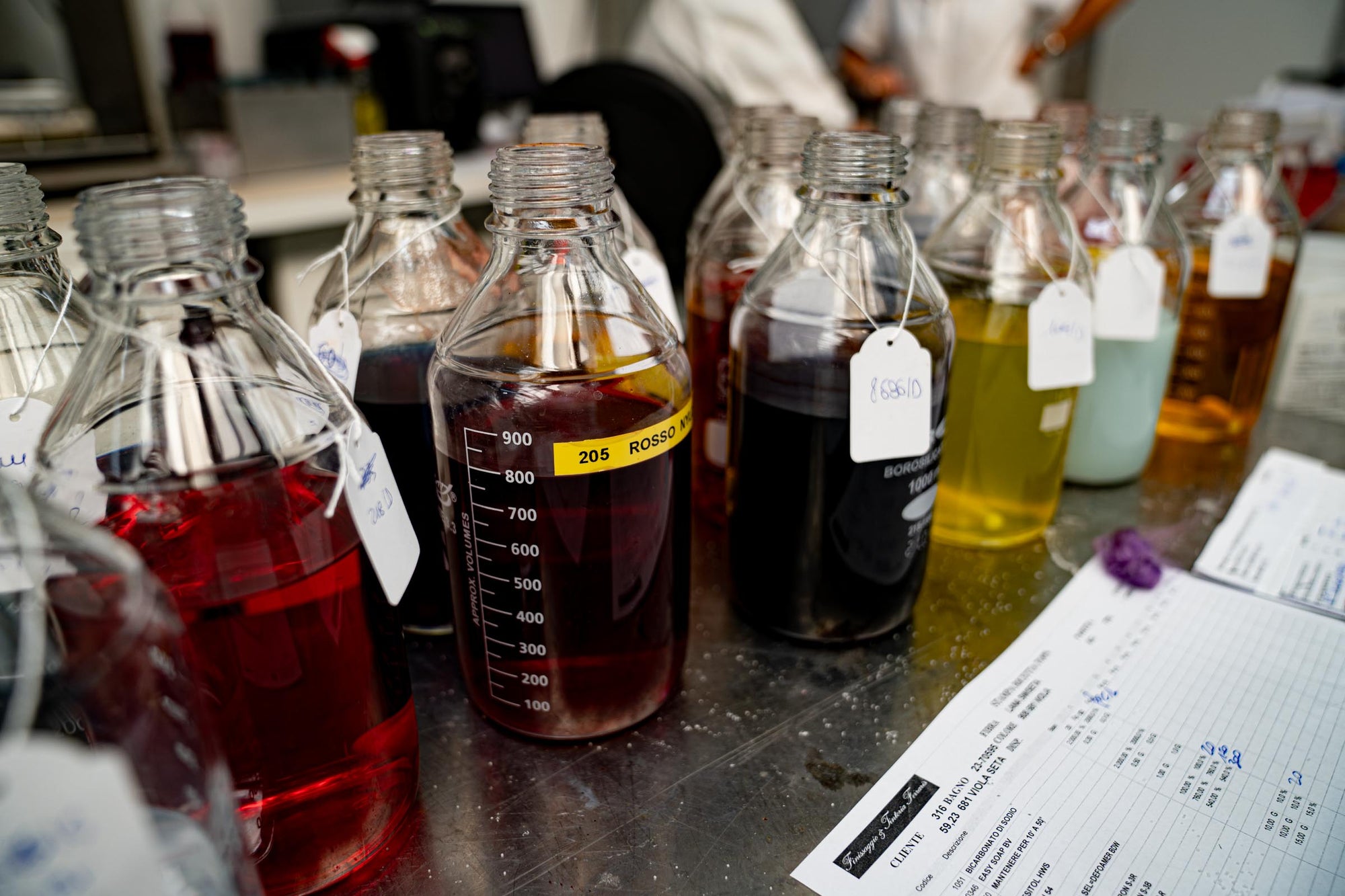 Close-up of bottles filled with dye colours on a table in the coloring lab of Tintoria Ferraris.