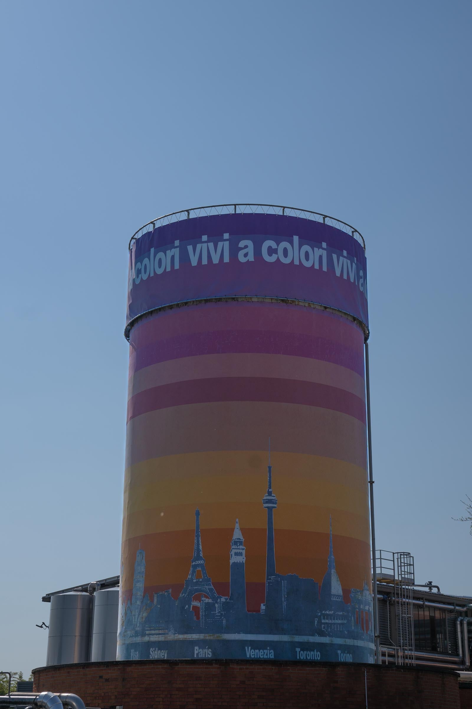 A water silo adorned with "Vico a colori" and vibrant purple and orange hues painted across the facility of Tintoria Ferraris.