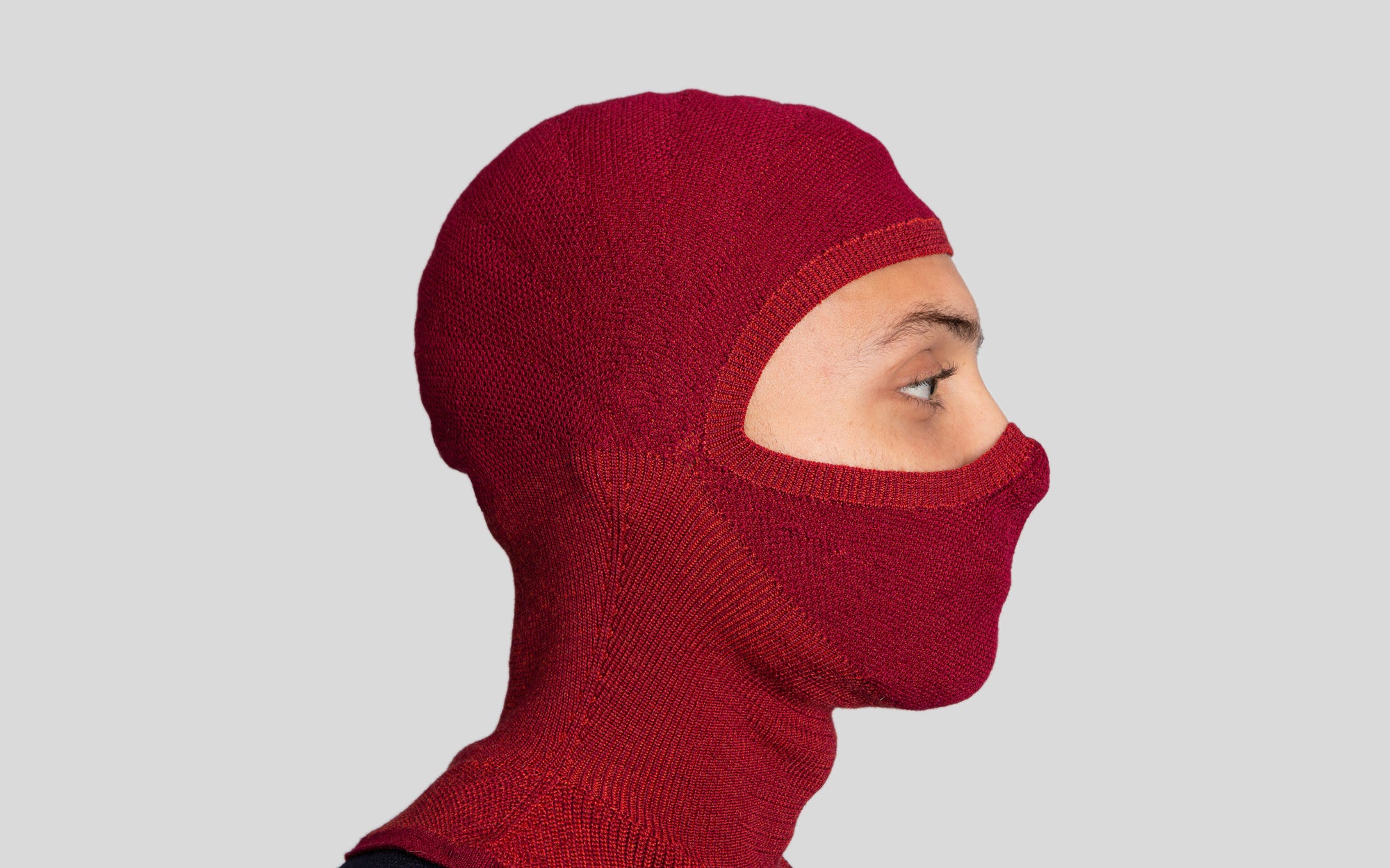 Side profile of model wearing The Merino Balaclava in brick red.