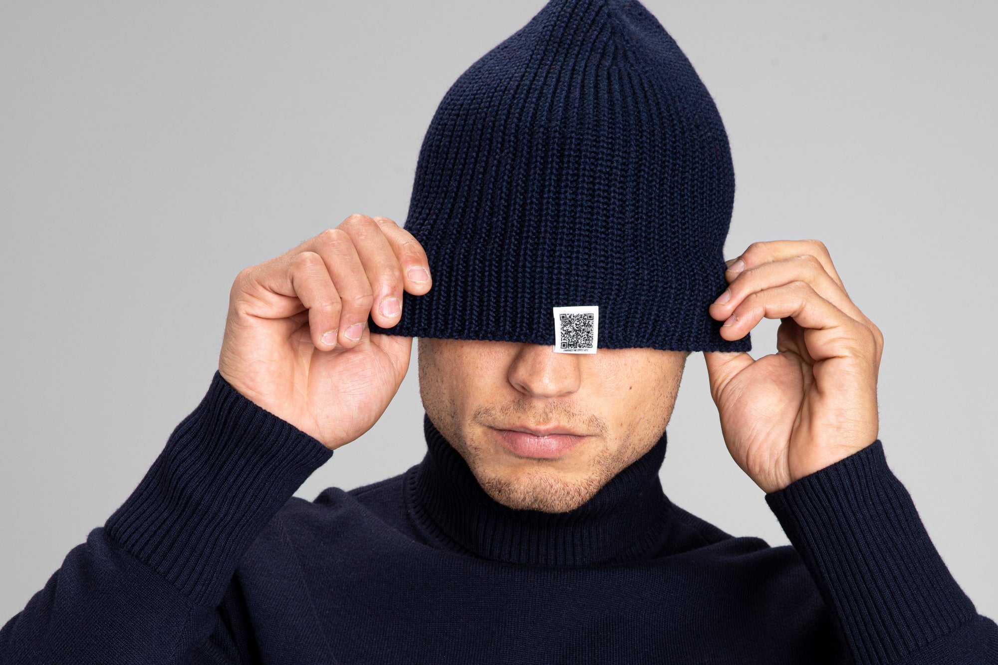 Model pulling down the edge o The Merino Beanie exposing the QR code 