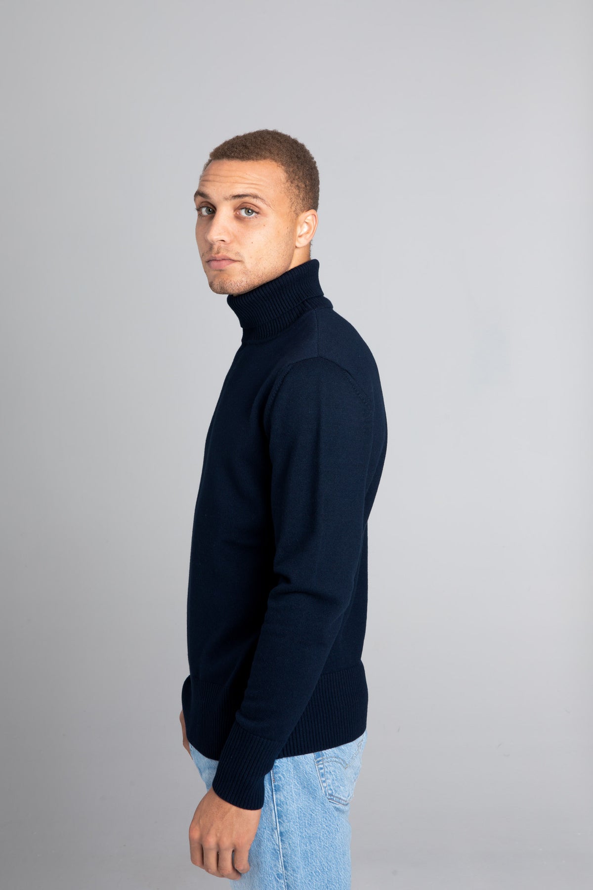 Model wearing The Merino Roll Neck Sweater Navy, left view - Unborn