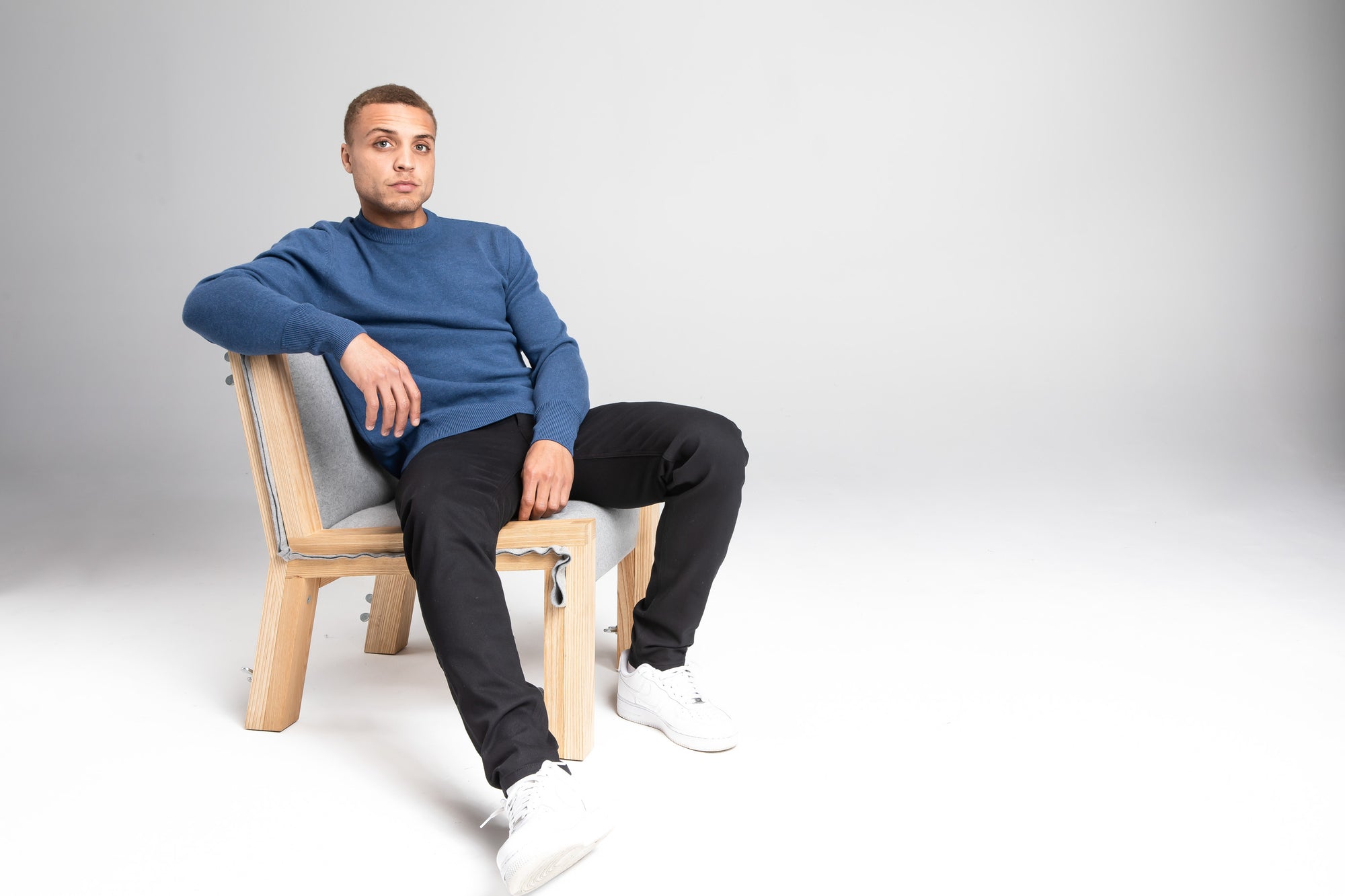 Model Wearing Merino Sweater Sky Blue Sitting Chair