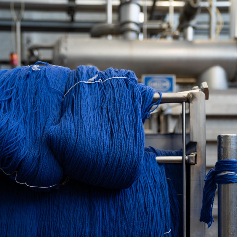 Blue hanks resting and drying on a metal rod at Tintoria Ferraris.
