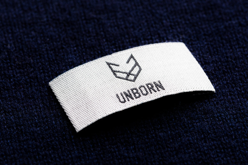 A white brand label from Unborn on top a navy Merino wool knitted fabric